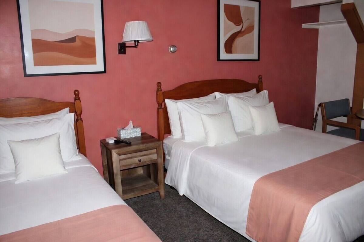 Habitación de hotel con dos camas, una mesita de noche con lámpara y cuadros en las paredes.