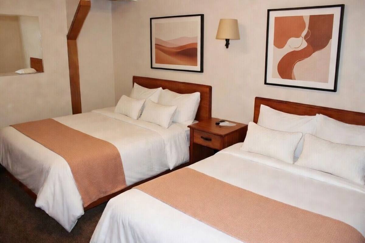 Habitación de hotel con dos camas, una mesita de noche, una lámpara y arte abstracto en la pared.