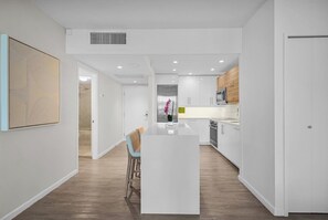 A modern kitchen with white cabinetry, a central island, and a dining area with a chair. - Direct Oceanfront + Balcony Suite in 5-Star Resort (Miami Beach)