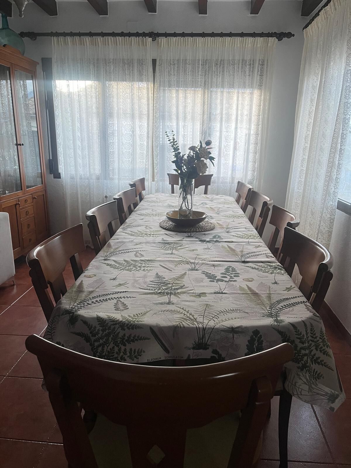 Un comedor con una mesa larga, sillas, un armario y cortinas.