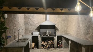 Een buitenkeuken van natuursteen met een barbecue, een spoelbak en een houtopslag.