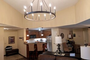 A modern kitchen with a central island, a dining area with a brown leather couch, and a living room with a lamp and a clock on the wall. - Top floor Family 3 Bed w/4 Bunks (Vernon Township)