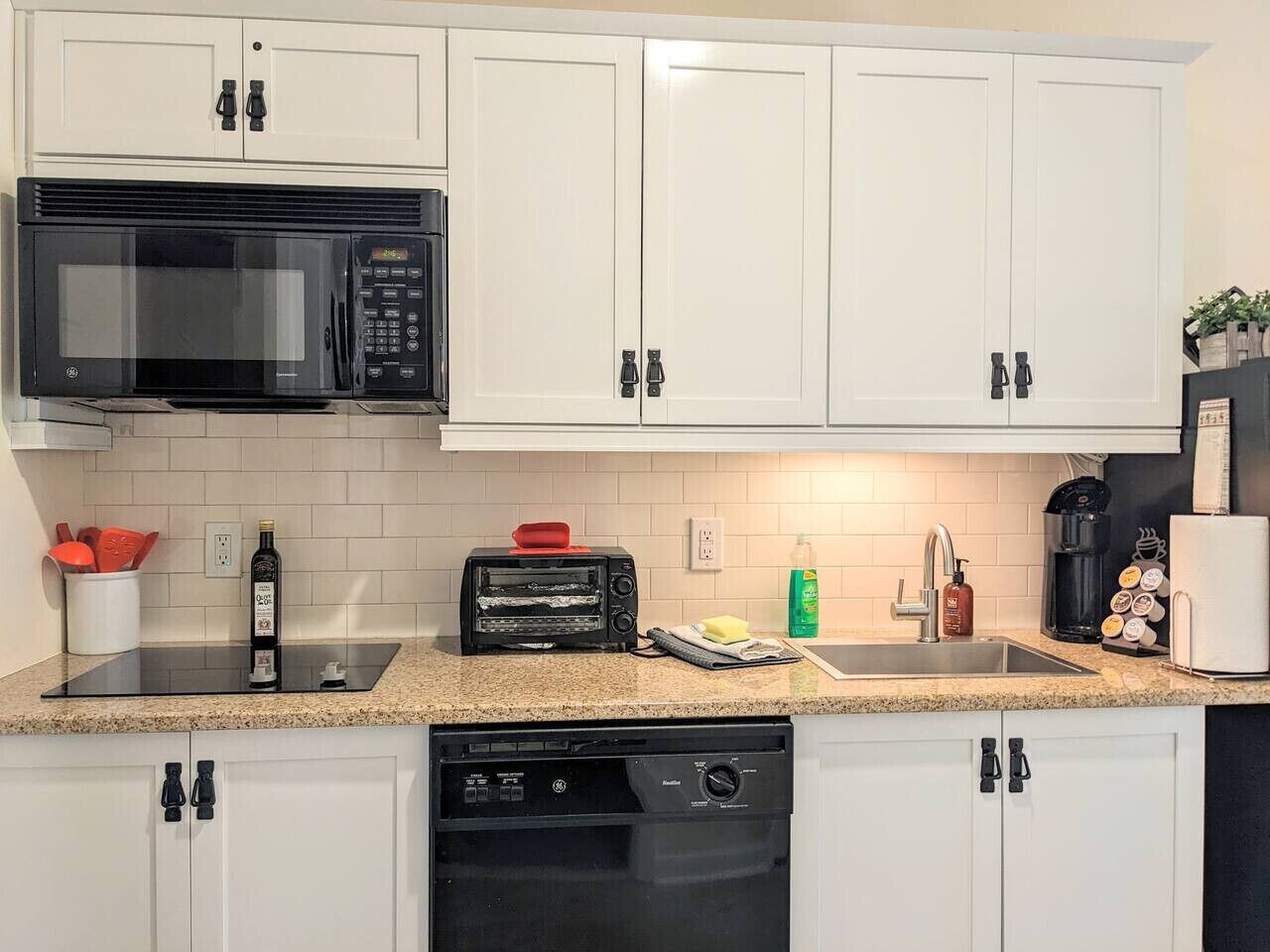A kitchen with white cabinets, a black microwave, a toaster, a sink, and a coffee maker.