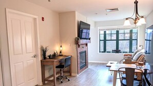 Ein Zimmer mit Kamin, Fernseher, Essbereich und großem Fenster.