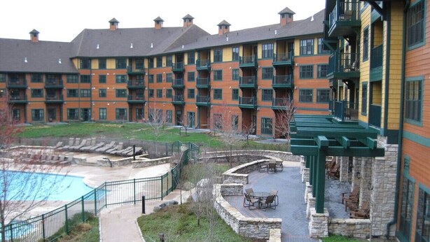 Ein mehrstöckiges Hotel mit Poolbereich, Außenbereich zum Sitzen und einem Kiesweg.