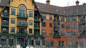 Ein mehrstöckiges Hotel mit Poolbereich, dessen Fassade gelbe und rote Bauteile sowie ein markantes A-förmiges architektonisches Element aufweist.