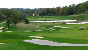 Ein Golfplatz mit Sandbunkern, einem Teich und einem Baum.