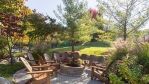 Een terras met houten stoelen en een ronde vuurplaats.