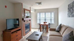Een woonkamer met televisie, open haard, eettafel en bank.