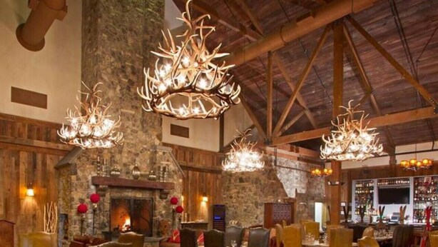Een restaurant met houten wanden, een stenen open haard en meerdere kroonluchters. Tafels zijn gedekt met borden en glazen.