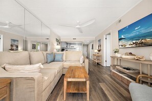 Ein geräumiges Wohnzimmer mit einem Holztisch, einem beigen Sofa und einem großen Gemälde von einer Strandansicht.