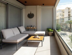 A balcony with a sofa, a wooden table, and potted plants. - GET Seaside Vibe Apartment Loutraki (Loutraki)