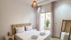 Une chambre moderne avec un grand lit, des tables de chevet, un luminaire suspendu et une vue sur l’extérieur.