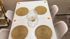 Une table carrée agrémentée de quatre sets de table en fibres tressées, d’un centre de table en verre et de bougies.