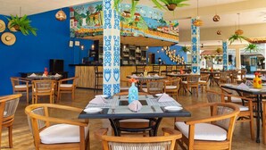 Ein Restaurant mit Holztischen, blauen Wänden und tropischen Pflanzen.