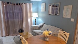 Un coin repas avec une table ronde en bois, des chaises, un vase de fleurs, un canapé, une lampe et une fenêtre avec des rideaux.