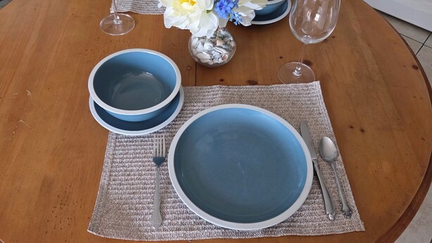 Une table à manger dressée avec de l’argenterie, des assiettes bleues et un vase rempli de fleurs.