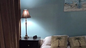 Une chambre à coucher avec un lit, une table de chevet, une lampe, un tableau au mur et un rideau.