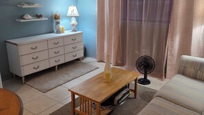 Un salon comprenant un canapé, une table basse en bois, une commode blanche et un ventilateur.
