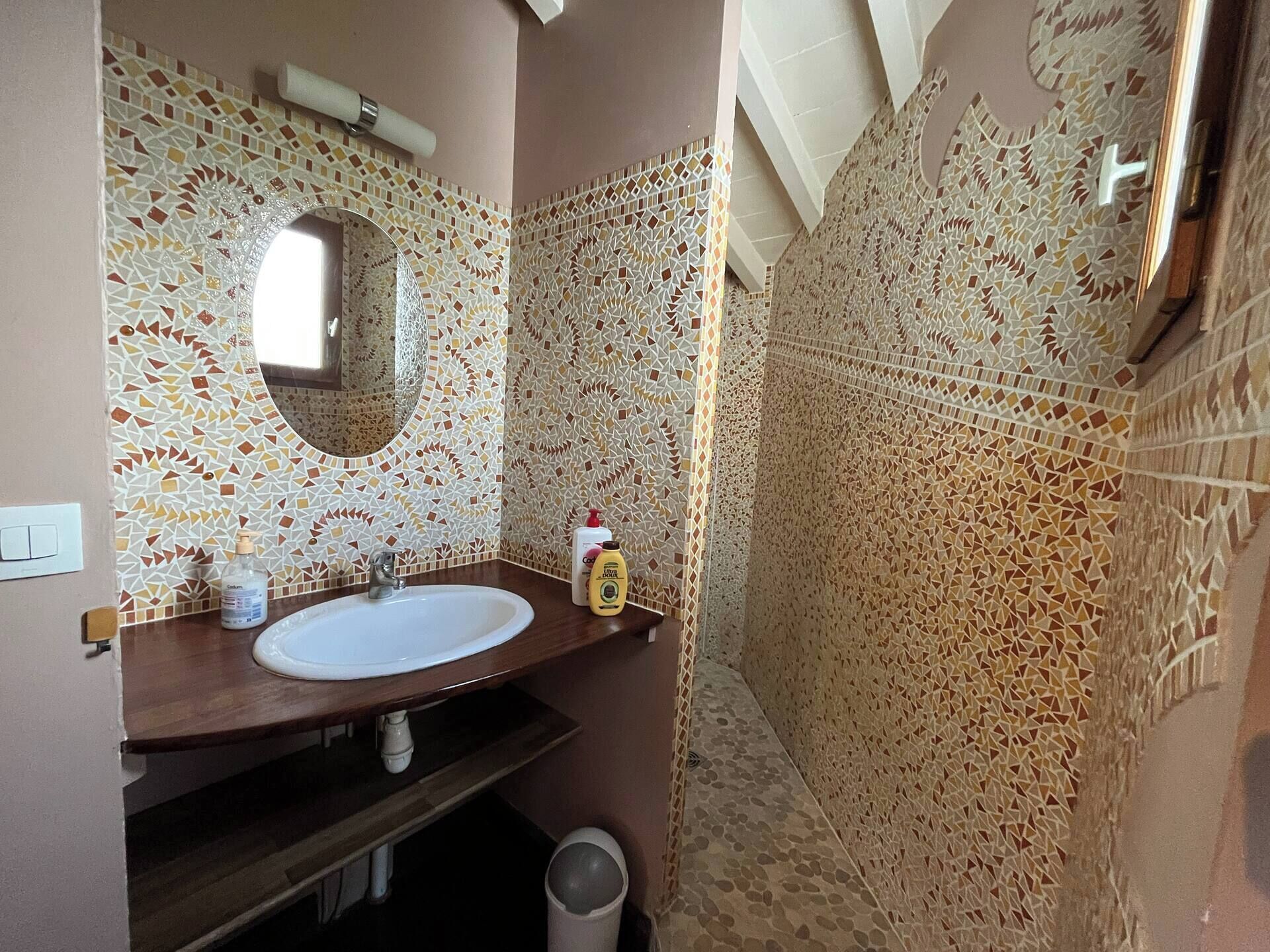 A bathroom with a mosaic tile wall, a sink, and a mirror.