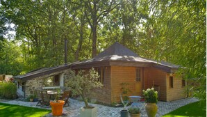Une cabane en bois avec une extension en pierre, entourée d’un jardin agrémenté de plantes en pot et d’une table de patio.