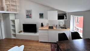 Een kleine keuken met een televisie, magnetron en spoelbak, houten vloer en een raam met uitzicht.