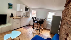 Een ruimtelijk ingerichte leefruimte met kitchenette, een eethoek, een bank en een televisie.