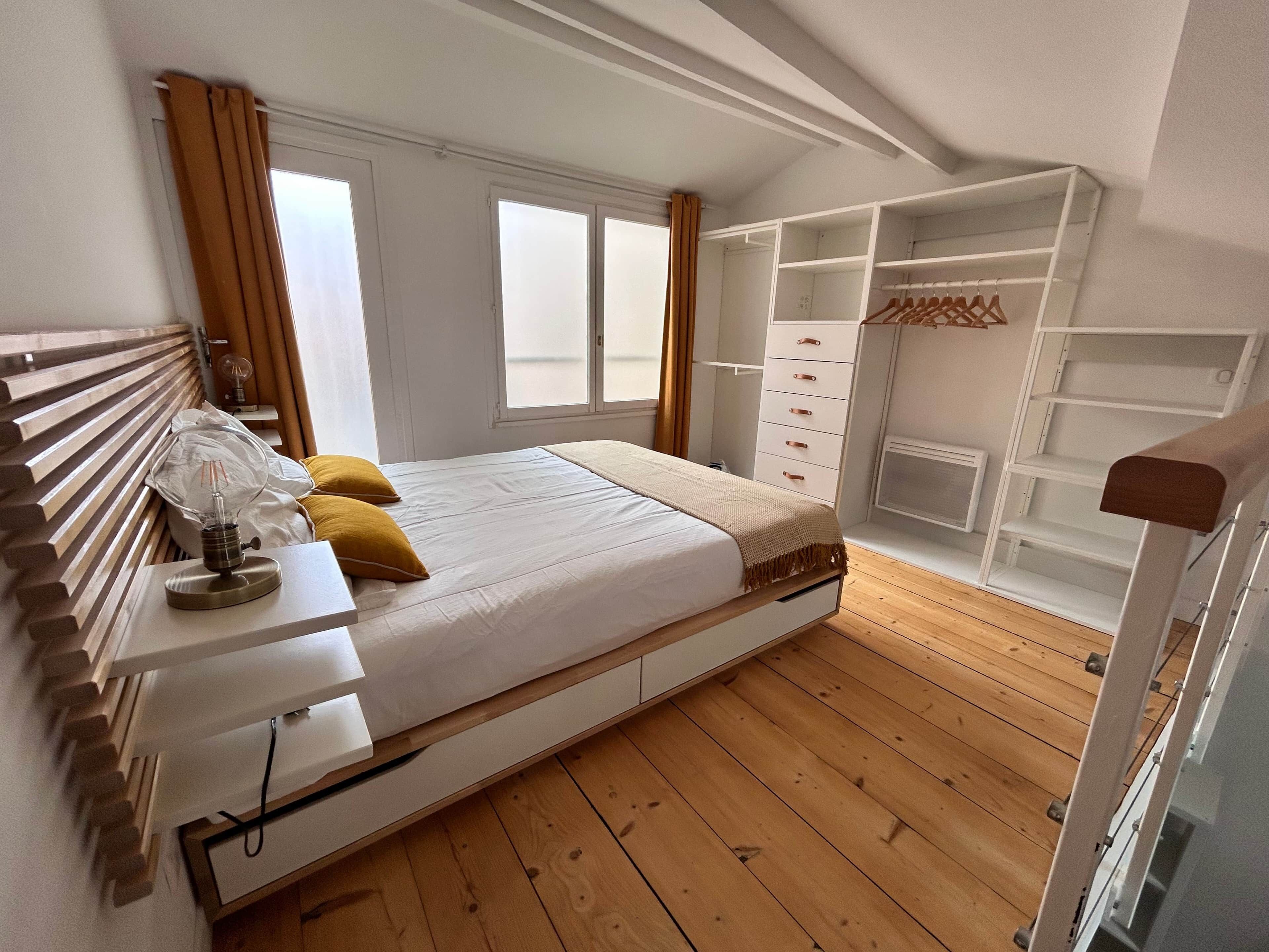 Een slaapkamer met een bed, nachtkastje, lamp en een kledingkast met planken.