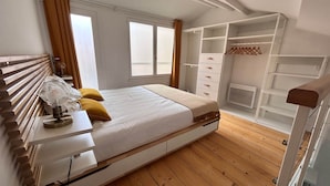 Een slaapkamer met een bed, nachtkastje, lamp en een kledingkast met planken.
