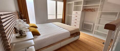 Une chambre à coucher comprenant un lit, une table de chevet, une lampe et une armoire avec des étagères.