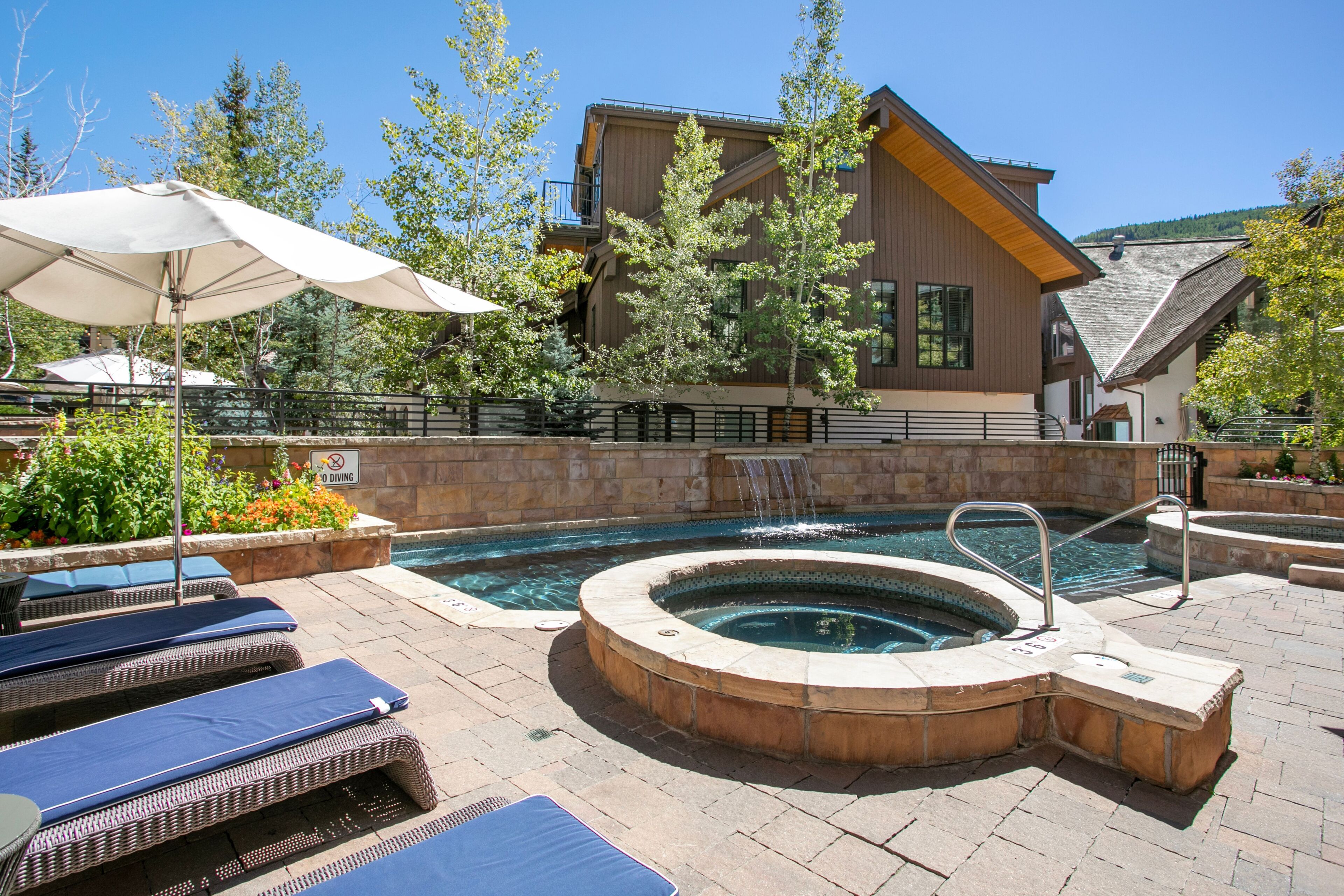 A pool area with lounge chairs, a hot tub, and a building with a wooden facade.