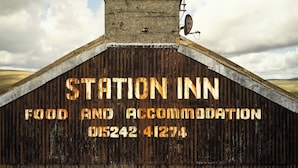 Ein rustikales Gebäude mit einem Schild, auf dem 'STATION INN FOOD AND ACCOMMODATION' und eine Telefonnummer stehen.