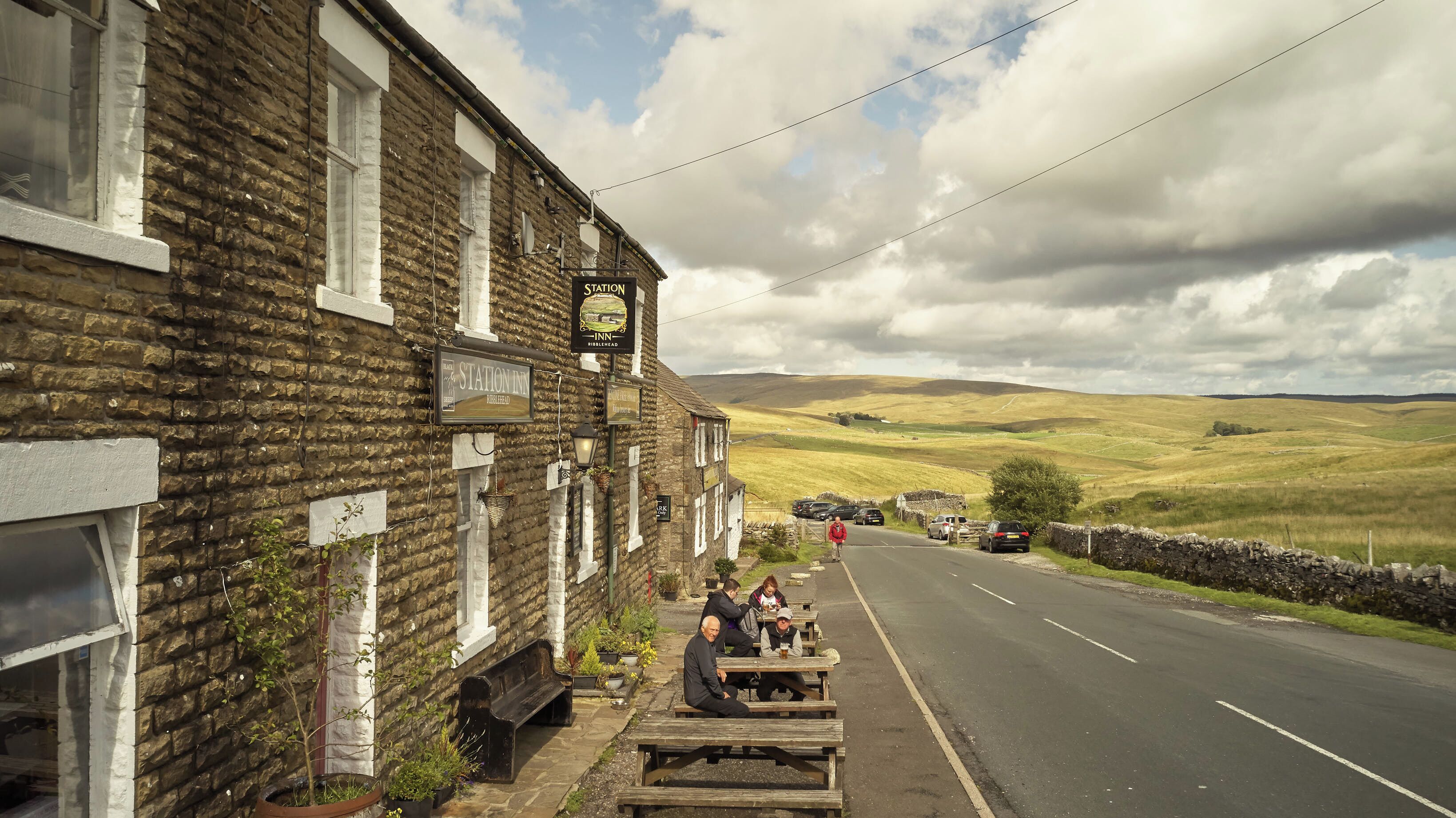 A stone building with a sign for 'Station Inn' and outdoor seating along a road.