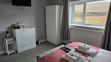 Habitación de hotel con cama, televisión, armario, una pequeña mesa con hervidor y ventana con vista a un puente.