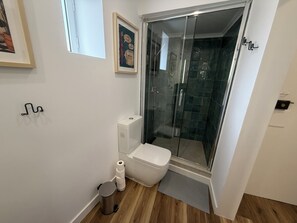 Ein modernes Badezimmer mit einer Duschkabine aus Glas, einer Toilette, einem Mülleimer und einem gerahmten Bild an der Wand.