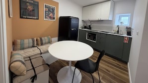 Ett kompakt bostadsutrymme med ett litet kök, en matplats med ett runt bord och stolar, en soffa med kuddar och två inspirerande affischer på väggen.
