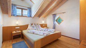 Un dormitorio con cama de madera, una mesita de noche, una lámpara de pared y un ventanal con cortinas.