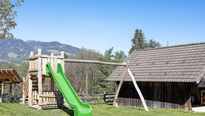 Un parque infantil con un tobogán verde, un columpio de madera y un edificio rústico con techo de tejas.