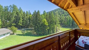 Un balcón de madera con vistas a una ladera boscosa y una zona cubierta de césped.