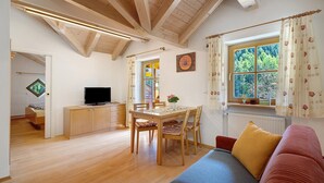 A room with a dining table, chairs, a sofa, a TV, and a window with curtains. - Apartment 'Getzenbergerhof' with Balcony and Wi-Fi (Chienes)