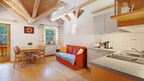 A kitchen with a wooden ceiling, a dining area with a table and chairs, a red sofa, and a window with curtains. - Apartment 'Getzenbergerhof' with Balcony and Wi-Fi (Chienes)