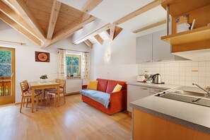 Eine Küche mit Holzboden, ein Essbereich mit Tisch und Stühlen, ein rotes Sofa und ein Fenster mit Vorhängen.