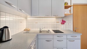 A modern kitchen with white cabinets, a stainless steel kettle, a sink, and a wooden door. - Apartment 'Getzenbergerhof' with Balcony and Wi-Fi (Chienes)