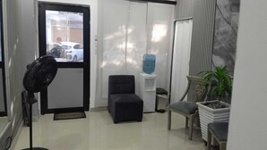 A room with a black fan, a small black chair, a water dispenser, and a potted plant. - Hostal Caimán del Rio (Barranquilla)