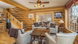 A log cabin interior with a wooden staircase, a sofa set, a coffee table, and a ceiling fan. - Hebgen Lakeshore Retreat (West Yellowstone)