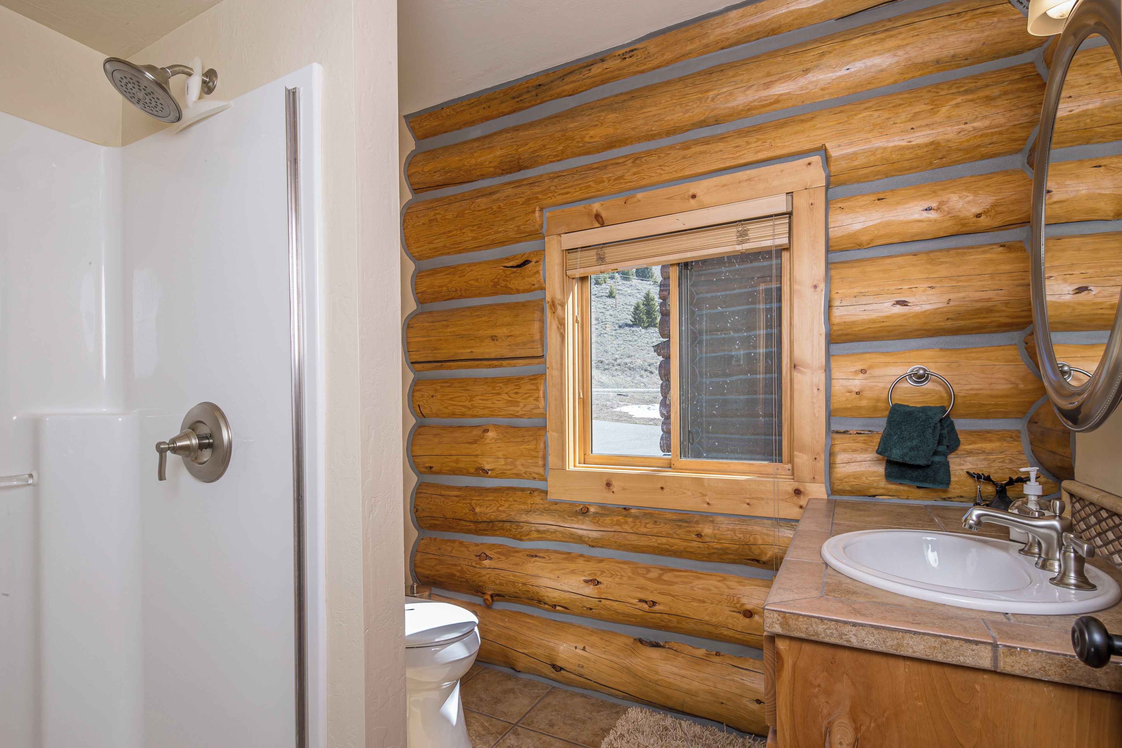 A bathroom with wooden walls, a window, a sink, and a shower.
