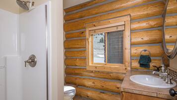 A bathroom with wooden walls, a window, a sink, and a shower.