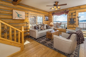 A log cabin interior with a sofa, armchair, and a dining table. - Hebgen Lakeshore Retreat (West Yellowstone)
