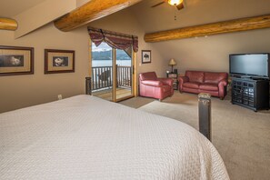 Ein Schlafzimmer mit einem großen Bett, einem roten Ledersessel, einem Fernseher und Blick auf einen See.