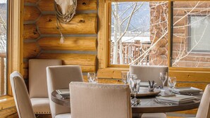 A wooden interior with a dining table set for four, chairs, and a large window with a view of bare trees. - Hebgen Lakeshore Retreat (West Yellowstone)